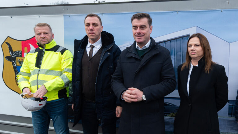 Grupa osób, w tym prezydent, pozuje na tle ścianki z wizualizacją obiektu.