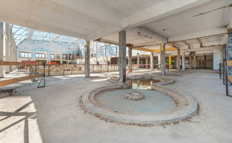 Widok przestrzeni basenowej w trakcie remontu - z rozebranym dachem i sprzętem budowlanym. Na pierwszym planie niegdysiejszy brodzik dla dzieci.