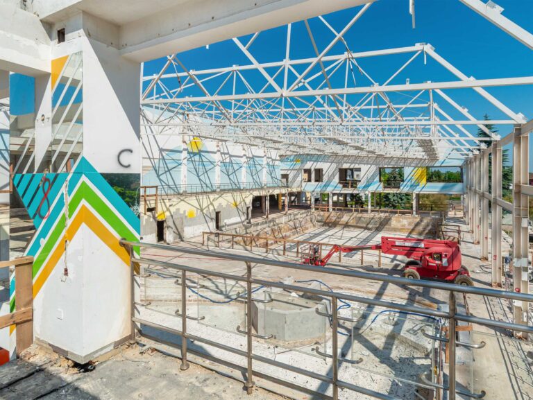 Widok przestrzeni basenowej w trakcie remontu - z rozebranym dachem i sprzętem budowlanym.